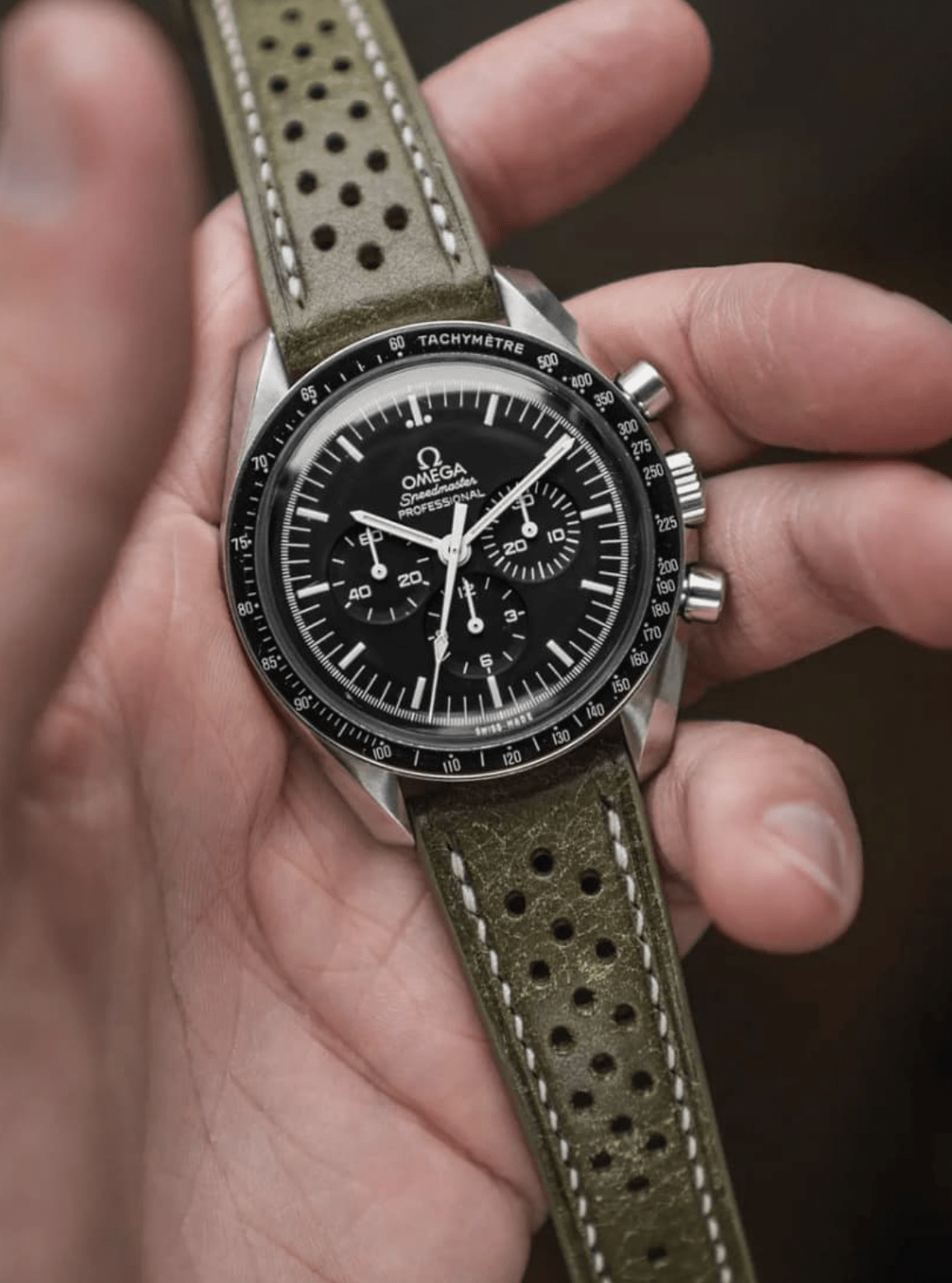 Close-up of a person holding a watch with a green leather strap.