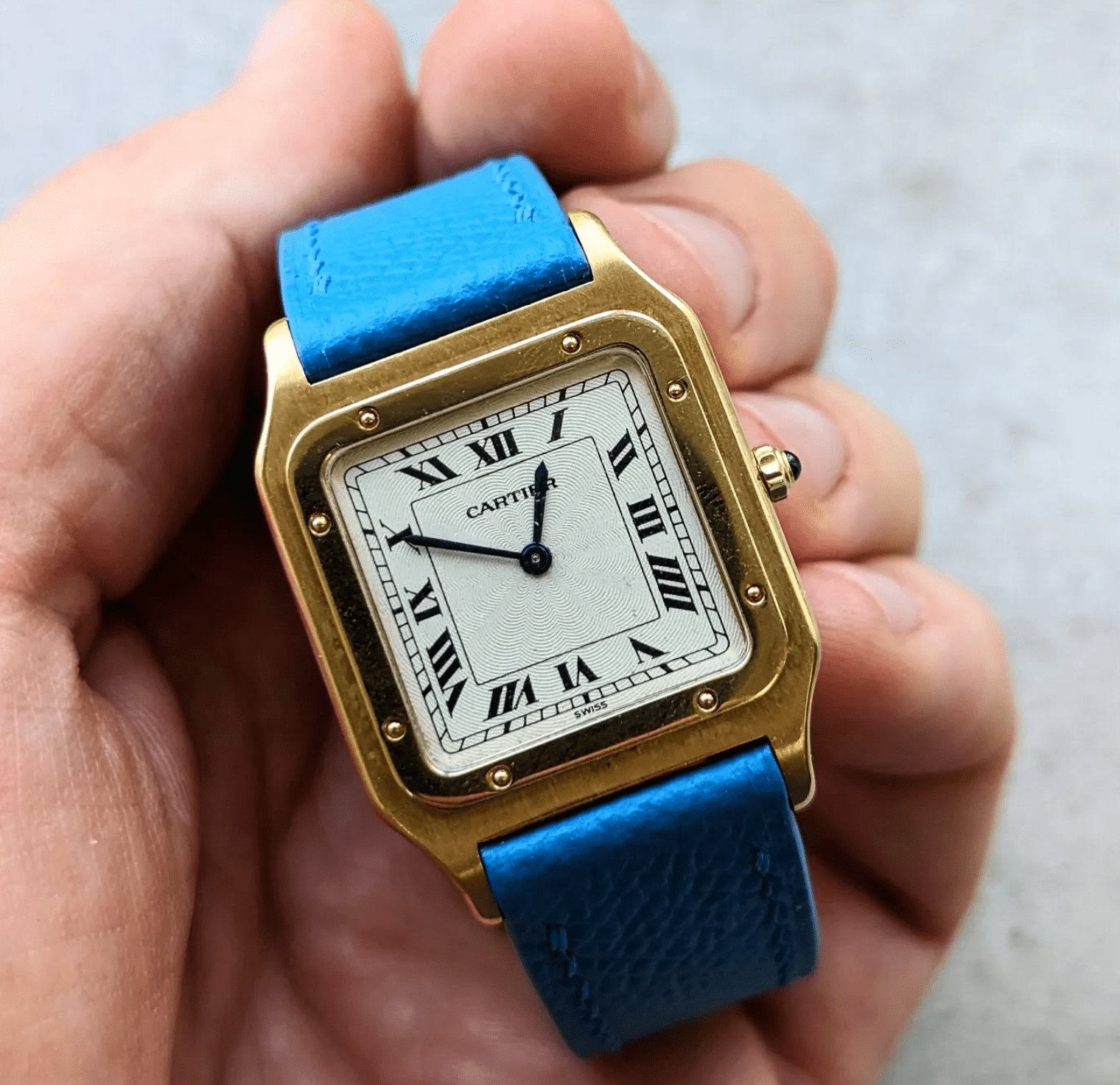 Gold Cartier watch with blue strap held in a hand