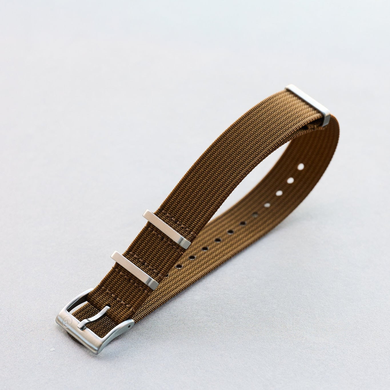 Brown watch strap with silver buckle on a light gray background