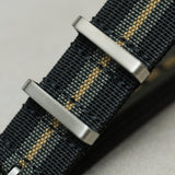 Close-up of a woven watch strap in black and gray with a thin gold stripe, featuring brushed silver metal buckle hardware.