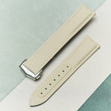 A light beige leather watch strap with a silver-toned metal buckle, laid diagonally on a split white and mint green background.