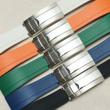 Four watch strap color options with silver-toned metal clasp, arranged diagonally on a light beige textured background. The straps are white, orange, green, blue, and black.