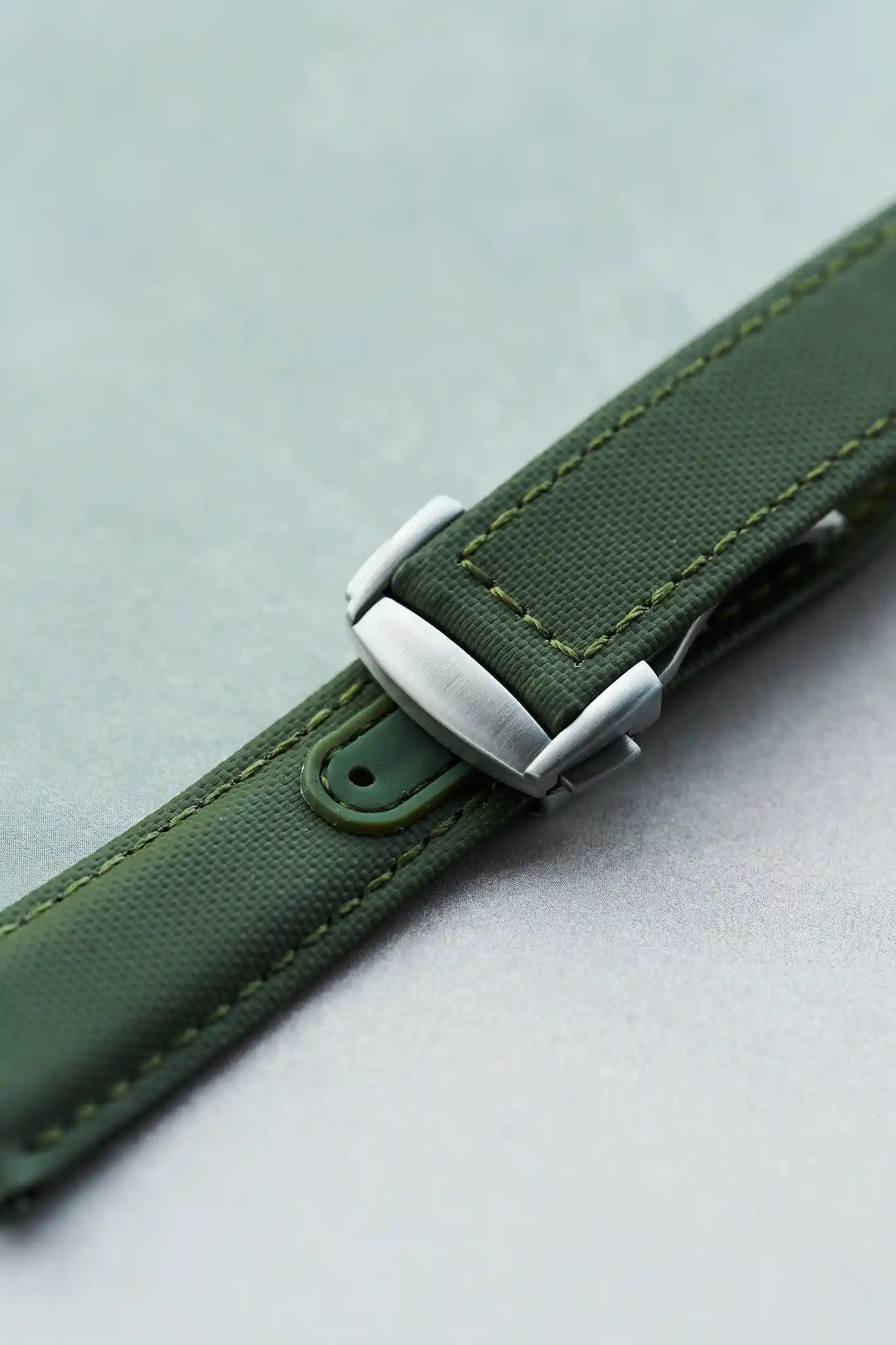 Green watch strap with silver buckle on a light gray background