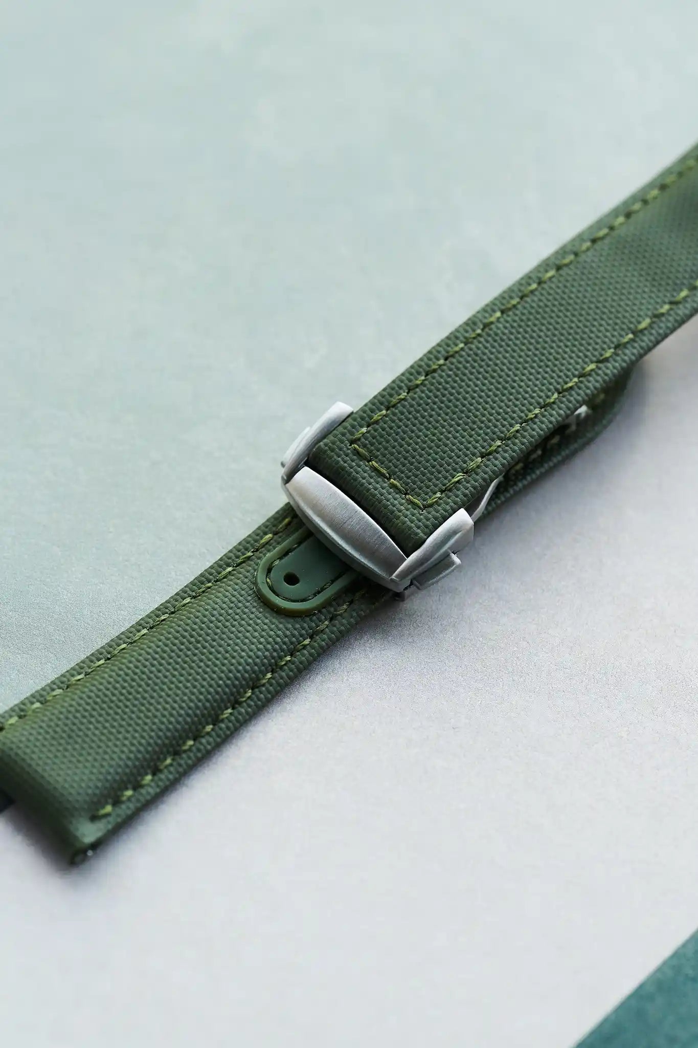 Green watch strap with silver buckle on a light gray background